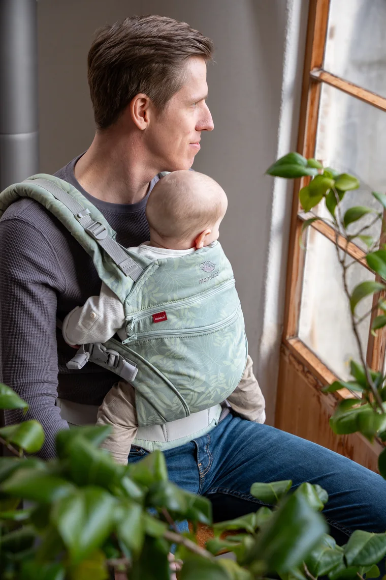 Vater mit Baby in der Trage am Fenster