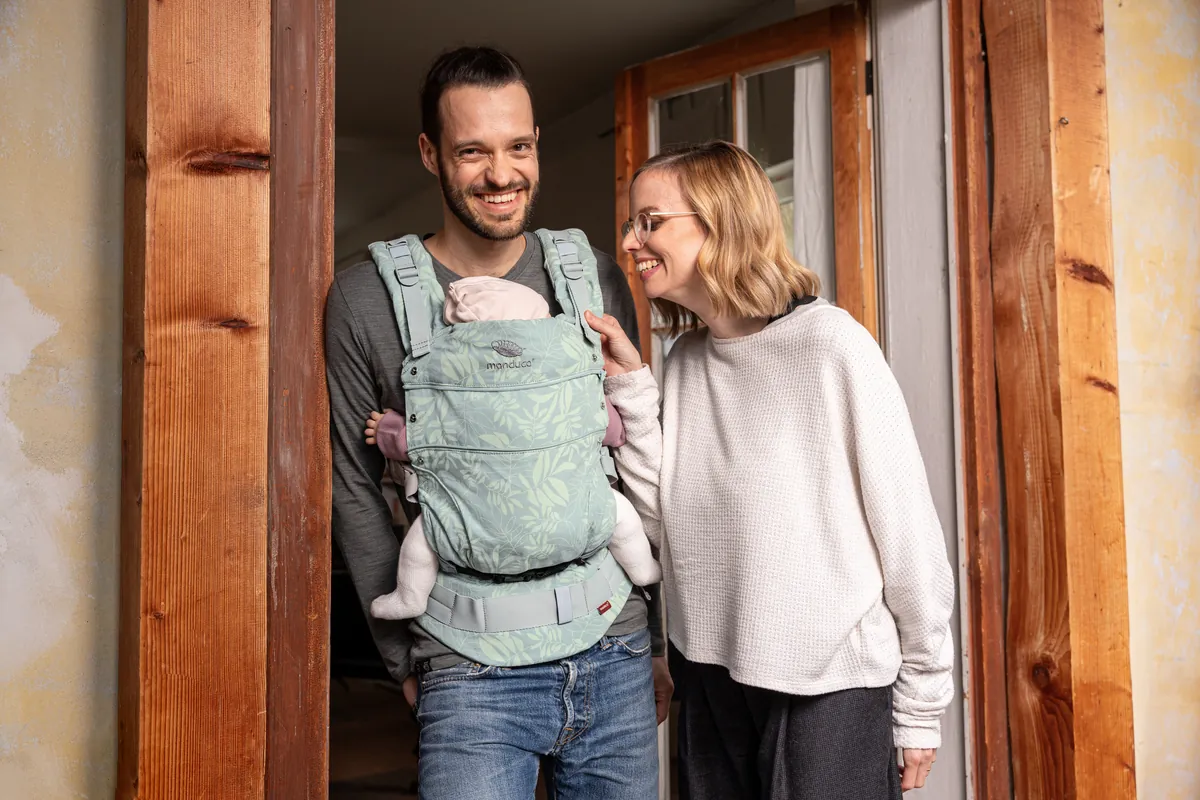Paar mit Baby in der Trage in einem Türrahmen