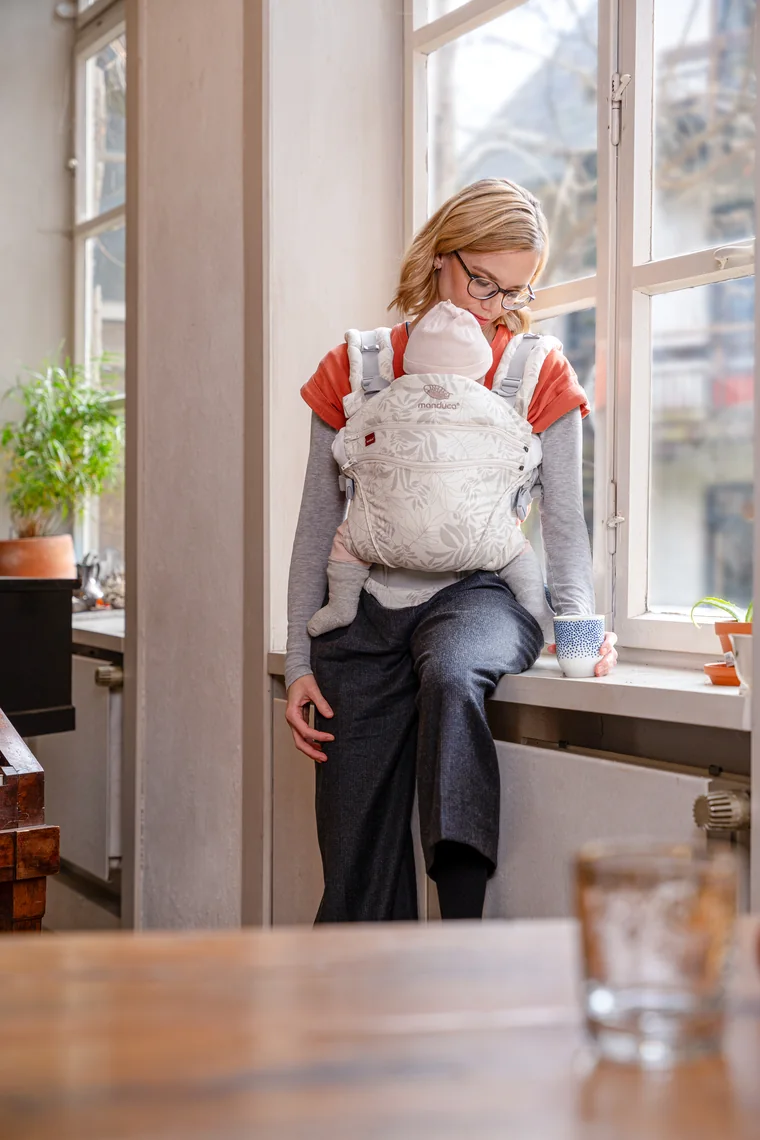 Mutter mit Baby in der Trage am Küchenfenster